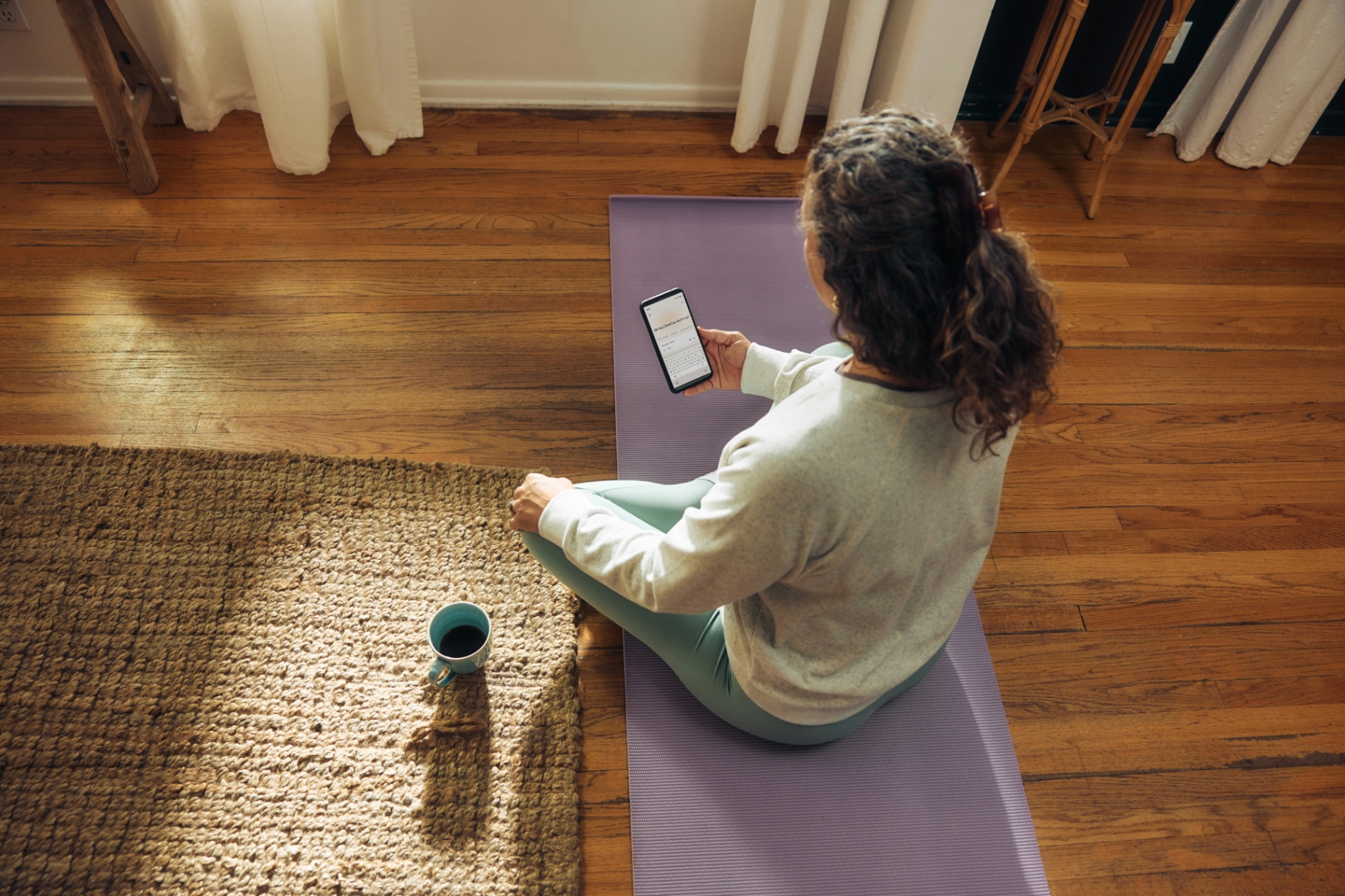 Person sitzt ruhig auf einer Yoga-Matte zu Hause und liest auf ihrem Smartphone